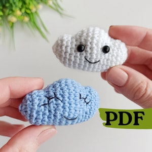 May include: Two crocheted cloud toys with smiling faces. One cloud is white and the other is light blue.