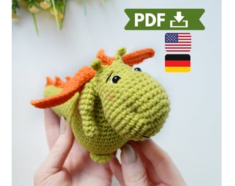 May include: Crochet pattern PDF for a green and orange dragon amigurumi toy. The pattern is available in English and German.