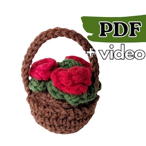 May include: A crocheted brown basket with a handle, filled with red roses and green leaves. The text "PDF + video" is in the upper right corner. This handmade item is perfect for home decor or as a unique gift.