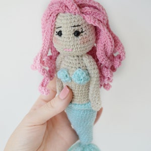 May include: A crocheted mermaid doll with pink hair, a light blue tail, and a light blue and white top.