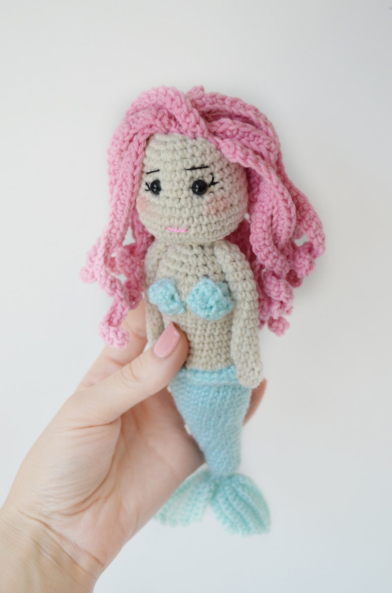 May include: A crocheted mermaid doll with pink hair, a light blue tail, and a light blue and white top.