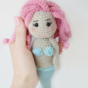 May include: A crocheted mermaid doll with pink hair, a light blue tail, and a light blue bikini top.