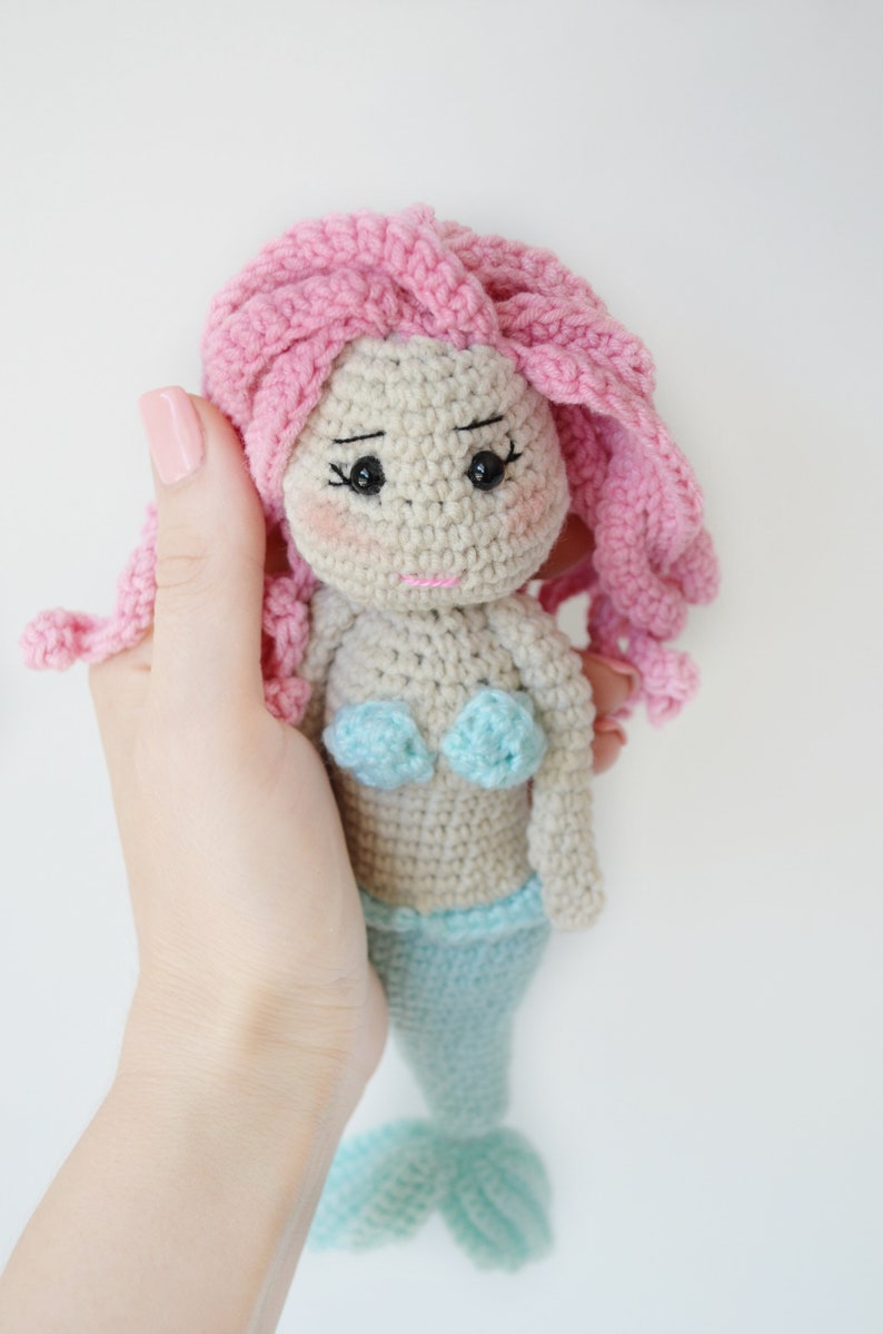 May include: A crocheted mermaid doll with pink hair, a light blue tail, and a light blue bikini top.