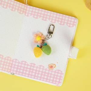 May include: A crocheted keychain with a yellow lemon, a green lime, and a pink flower charm. The keychain is attached to a silver metal ring.