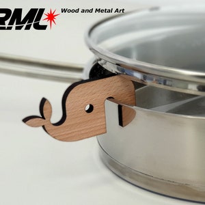 May include: A wooden whale-shaped pot lid holder in natural wood with black accents. The holder is attached to a stainless steel pot with a glass lid.