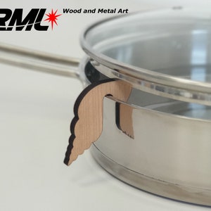 Può includere: Una pentola in acciaio inossidabile con coperchio in vetro e un porta coperchio in legno. Il porta coperchio in legno è marrone chiaro e ha una forma decorativa. Il testo "RML Wood and Metal Art" è nell'angolo in alto a sinistra.