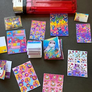 May include: A collection of miniature notebooks, stickers, and a small folder with colorful, whimsical designs. The designs include pandas, a leopard, and other vibrant illustrations. A red lighter is also present.