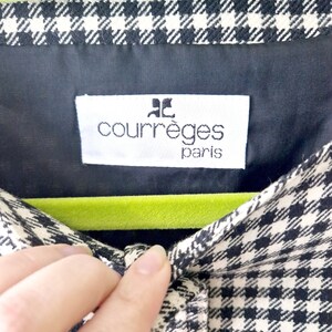 Op de afbeelding: Een shirt van zwart-wit gingham stof met een groene fluwelen hanger en een wit label met de tekst "Courr&egrave;ges Paris".