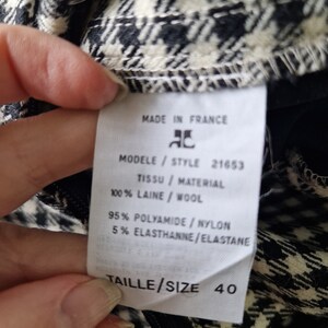 Op de afbeelding: Een wit label met zwarte tekst op een zwart-wit geruite stof. Het label vermeldt "Made in France", "Modele/Style 21653", "Tissu/Material 100% Laine/Wool", "95% Polyamide/Nylon 5% Elasthanne/Elastane", en "Taille/Size 40".