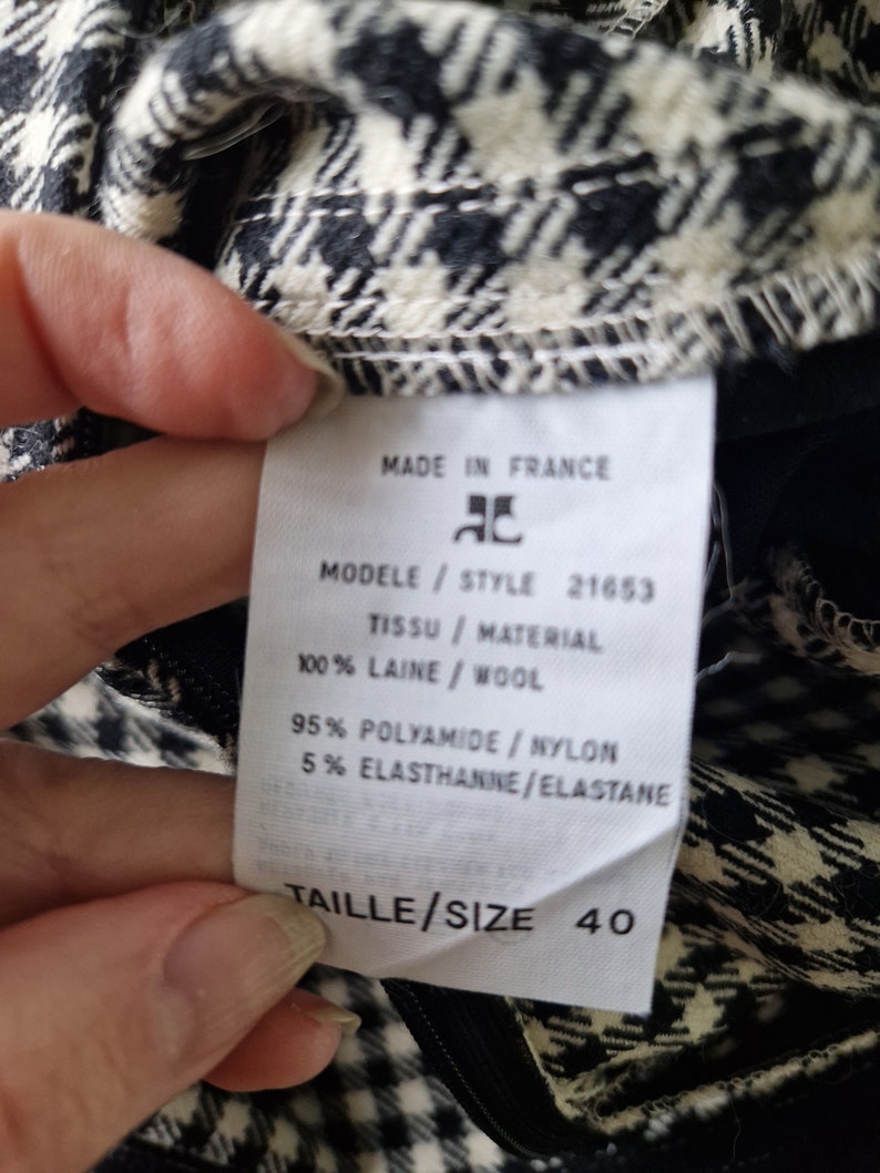 Op de afbeelding: Een wit label met zwarte tekst op een zwart-wit geruite stof. Het label vermeldt "Made in France", "Modele/Style 21653", "Tissu/Material 100% Laine/Wool", "95% Polyamide/Nylon 5% Elasthanne/Elastane", en "Taille/Size 40".