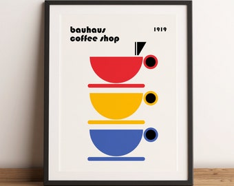 May include: A framed print with a Bauhaus coffee shop logo. The logo features three stacked cups in red, yellow, and blue, with black handles and a black 1919.