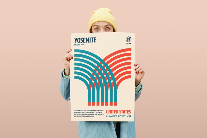 May include: A poster featuring a graphic design with red and teal lines, with the text "YOSEMITE NATIONAL PARK" and "UNITED STATES". The poster has a cream background and is held by a person wearing a yellow beanie and blue blazer.