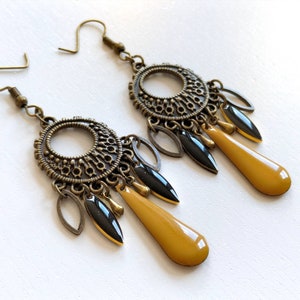 May include: A pair of gold-toned dangle earrings with black and yellow accents. The earrings feature a round, ornate design with multiple dangling charms.