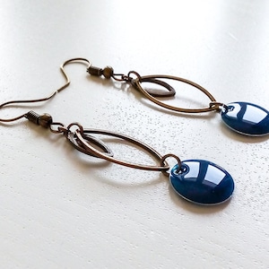 Puede incluir: Un par de pendientes colgantes con una piedra ovalada azul y un diseño de metal dorado.
