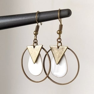 Peut inclure: Une paire de boucles d'oreilles créoles dorées avec un pendentif blanc en forme de larme et un charme triangle doré.