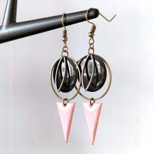 Pode incluir: Um par de brincos pendentes com um charme triangular rosa e um charme esférico preto e prata.