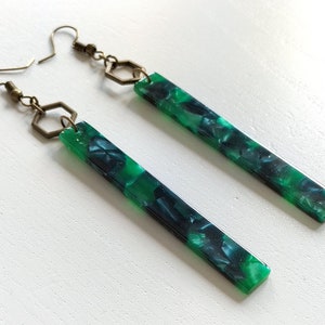 Peut inclure: Une paire de longues boucles d'oreilles vertes et noires avec un charme hexagonal et une fermeture à crochet.