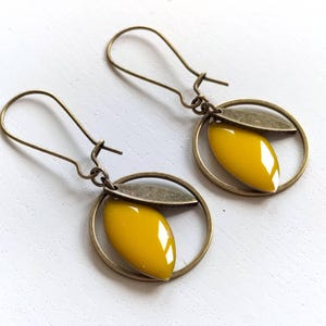 May include: A pair of gold-toned earrings with a yellow enamel leaf design. The earrings are made of metal and have a simple, elegant style.