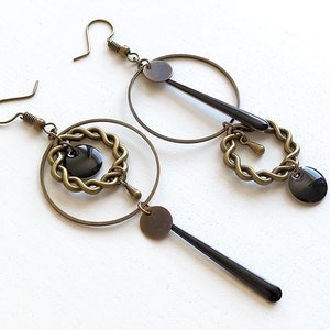 May include: A pair of gold-toned earrings with black accents. Each earring features a circle with a smaller circle inside, a dangling black rod, and a black disc.