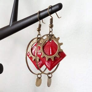 May include: Red and gold earrings with a gear design and a diamond-shaped pendant.