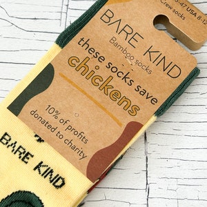 May include: A pair of yellow socks with a green and brown chicken design. The socks are made of bamboo and are part of the Bare Kind brand. The packaging says "these socks save chickens" and "10% of profits donated to charity".