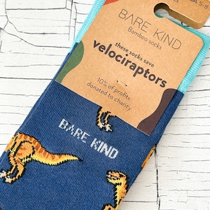 以下が含まれることがあります： 黄色いヴェロキラプトルの模様がついた青いクルーソックス。ソックスは竹から作られており、利益の10％は慈善団体に寄付されます。タグには「BARE KIND Bamboo socks these socks save velociraptors 10% of profits donated to charity」と書いてあります。