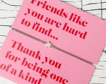 Puede incluir: Una tarjeta rosa con el texto "Friends like you are hard to find..." y "Thank you for being one of a kind." Una pulsera con dije de estrella plateada está colocada sobre la tarjeta. Las palabras "LETTERBOX LOVE" están en la parte inferior de la tarjeta.