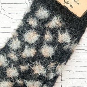 Pode incluir: Luvas sem dedos pretas e cinzentas com um padrão de bolinhas. As luvas têm uma textura macia e difusa e uma etiqueta que diz "Funky Fingerless Gloves". As luvas são projetadas para manter as mãos aquecidas, deixando os dedos livres.