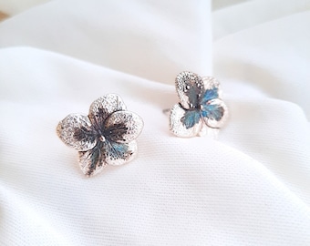 May include: A pair of silver flower-shaped earrings with blue accents. The earrings are delicate and feminine.