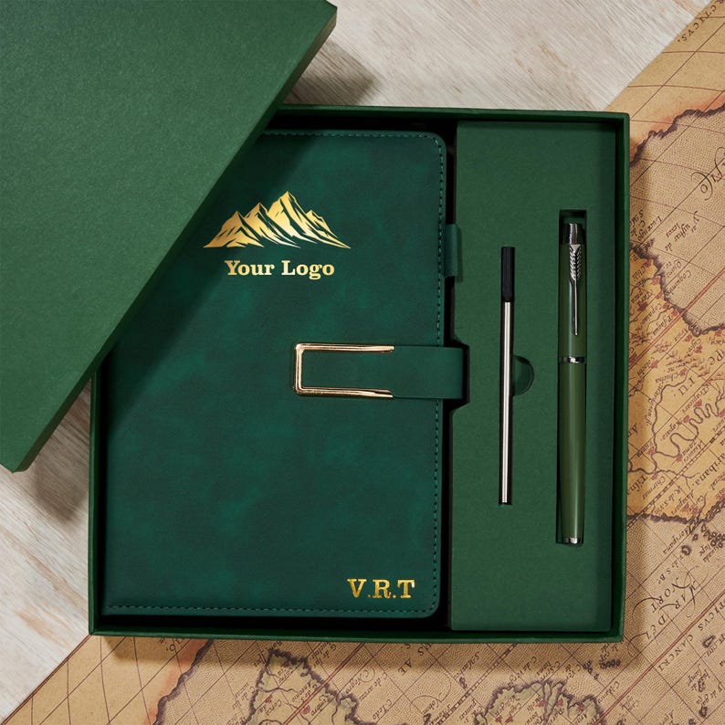 May include: A dark green journal and pen set in a gift box. The journal has a gold clasp and the text "Your Logo" and "V.R.T." The pen and journal are in a dark green box with a matching lid.