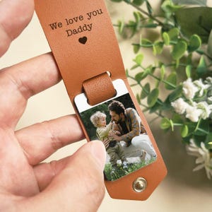 May include: A brown leather luggage tag with a photo insert. The photo shows a father and son. The tag has the text "We love you Daddy" engraved on it.
