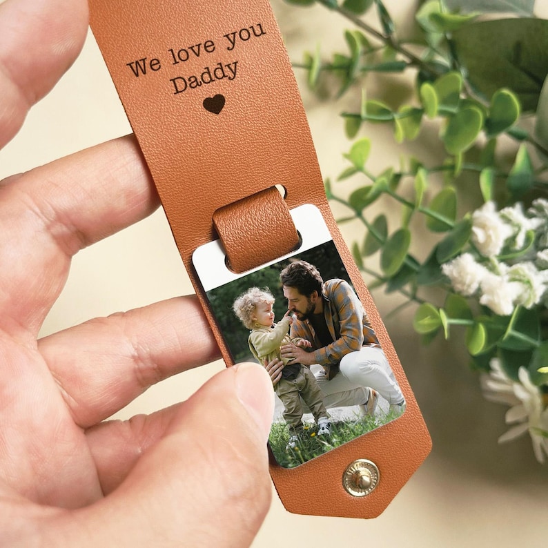 May include: A brown leather luggage tag with a photo insert. The photo shows a father and son. The tag has the text "We love you Daddy" engraved on it.