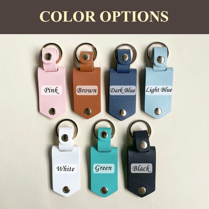 May include: Seven leather keychains in different colors: pink, brown, dark blue, light blue, white, green, and black. Each keychain has a metal ring and a small leather tag with the color name written on it.