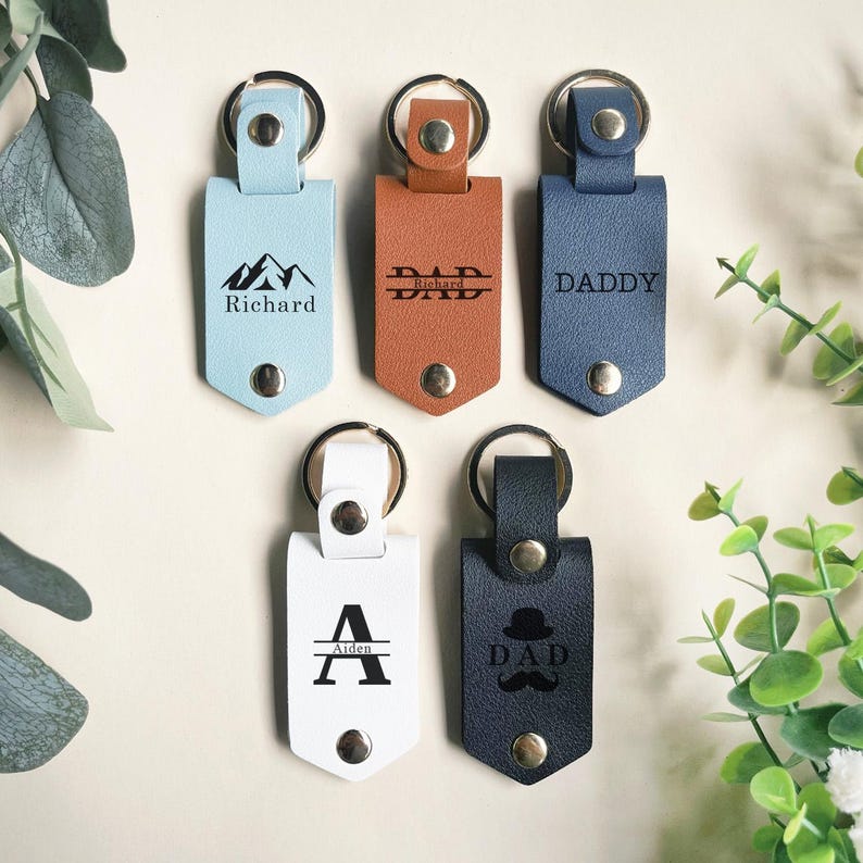 May include: Five leather keychains with different designs and text. The keychains are blue, brown, white, and black. The text on the keychains includes "Richard", "DAD", "DADDY", "Aiden", and "DAD".