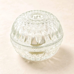 May include: A clear glass orb-shaped container featuring a textured diamond-cut pattern across its surface. The object consists of two halves that join at a central horizontal band, with a circular opening at the top of the upper dome section.
