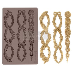 May include: A silicone mold with three floral garland designs. The mold is gray and the designs are raised. The mold is next to a gold-colored example of the garland designs.