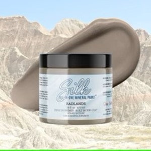 May include: A jar of Silk Mineral Paint in the colour "Badlands", a light brown with a hint of grey. The jar is labelled with the brand name and colour name.
