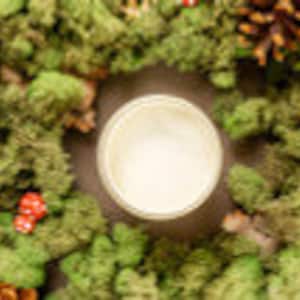 May include: A white candle in a glass jar surrounded by a green moss wreath with pine cones.