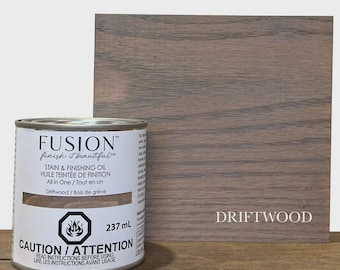 May include: A can of Fusion stain and finishing oil in Driftwood, with a wooden sample. The can has a white label with black text, including "CAUTION / ATTENTION" and "237 ml". The wooden sample is a rectangular shape with the word "DRIFTWOOD" on it.