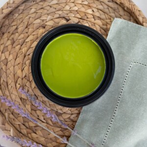 May include: A close-up of a green paint can with a black lid. The can is sitting on a woven wicker tray with lavender sprigs.