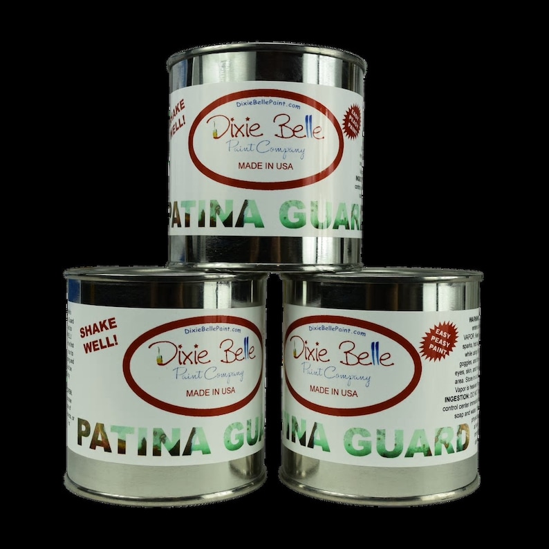 Op de afbeelding: Drie zilveren blikken Dixie Belle Patina Guard verf. De blikken zijn gelabeld met het Dixie Belle logo en de woorden "Patina Guard" in rood en groene letters. De blikken zijn op elkaar gestapeld.