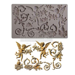 May include: A gray silicone mold featuring cherubs, roses, and ornate scrollwork. The design includes two cherubs with wings, floral arrangements, and decorative flourishes. Below, a golden-colored example of the design is shown.