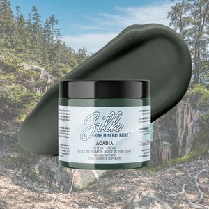 May include: A 473 ml jar of Silk All-in-One Mineral Paint in the colour Acadia. The paint is a dark green colour and the jar has a black lid. The text on the jar reads "Silk All-in-One Mineral Paint", "Acadia", "16 fl oz 473 ml", "Built in Primer - Built in Top Coat", "Vernis Intégre", and "Con Cubierta Superior".