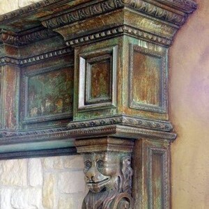 Op de afbeelding: Een close-up van een decoratieve schouw met ingewikkelde houtsnijwerk en een groene en bruine patina. De schouw heeft een gegraveerd leeuwenhoofd in de rechterbenedenhoek.