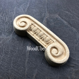 May include: A wooden scroll with a decorative design, featuring a series of rounded shapes and a spiral at each end. The scroll is a light beige color and has a smooth, polished finish.