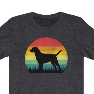 May include: Dark gray t-shirt featuring a silhouette of a dog standing in grass against a retro sunset. The sunset has bands of red, orange, yellow, and green. A stylish graphic tee for dog lovers.