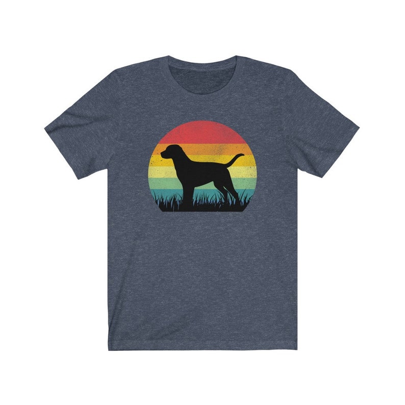 May include: A navy blue t-shirt featuring a black silhouette of a dog standing in front of a sunset. The sunset design includes bands of red, orange, yellow, and green. The dog is standing in front of a patch of green grass.