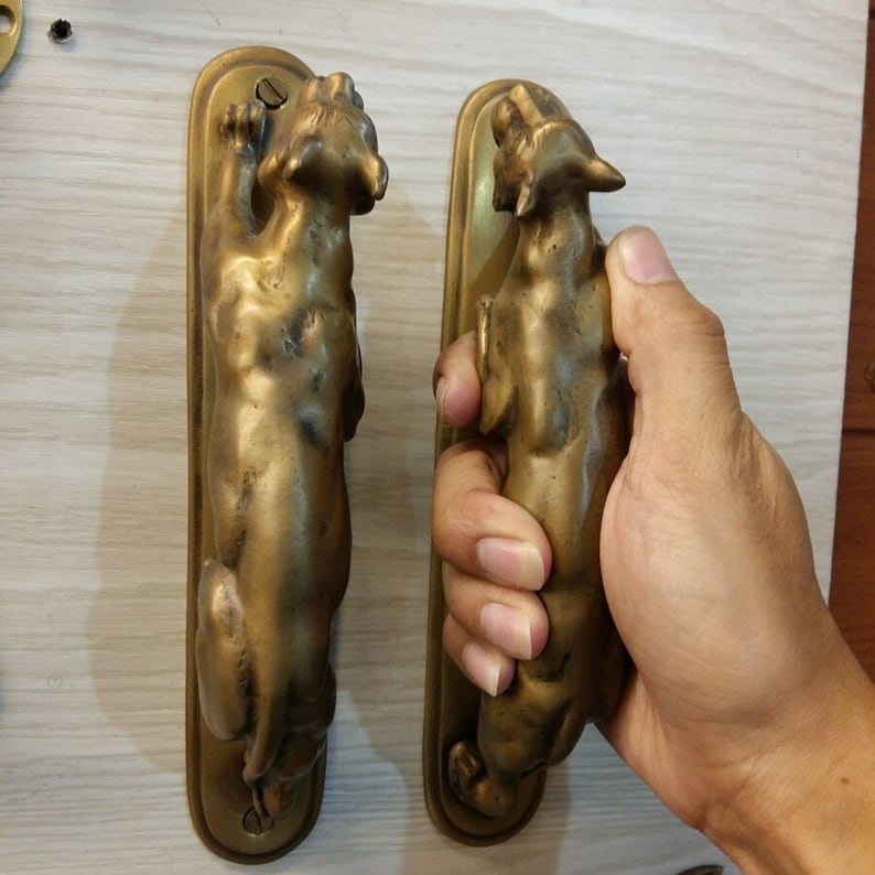 May include: A pair of antique brass door handles shaped like crouching panthers. The handles are mounted on rectangular plates.