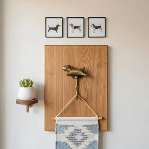 May include: A decorative wall arrangement with a dog theme. It includes three framed dog prints, a brass dog-shaped hook, a small woven tapestry with blue and white patterns, and a small wooden shelf with a potted succulent.