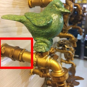 May include: A gold-colored metal garden hose faucet with a green bird figurine on top. The faucet has a threaded connector on the end.